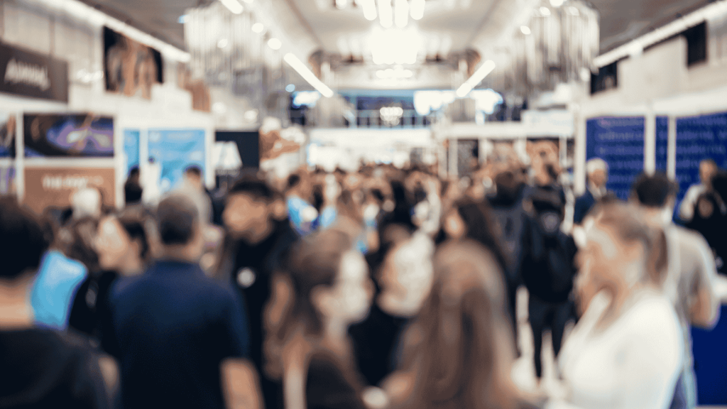 Público caminhando por um corredor de feira de tecnologia, com estandes nas laterais e ambiente movimentado, representando networking e inovação em eventos de tecnologia de 2026.